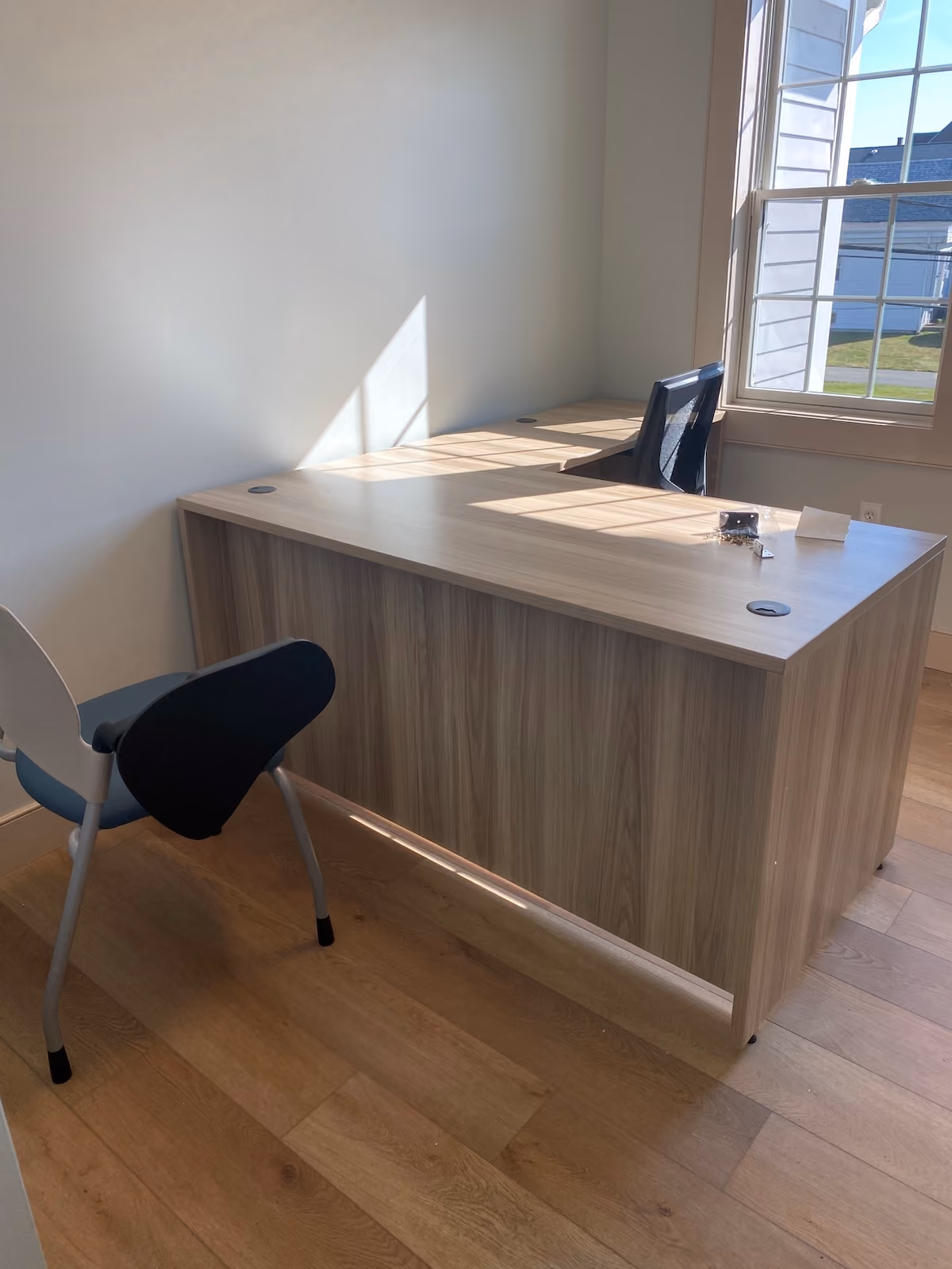 Private office in residential treatment center with large wooden desk, mesh office chair, and natural light from large window