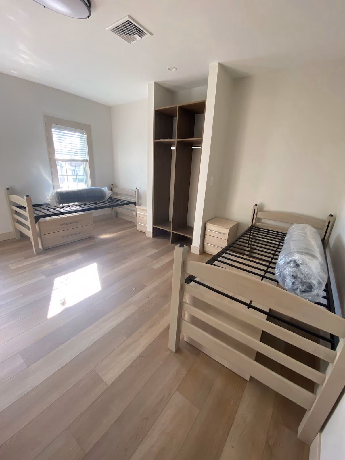Bright residential treatment facility bedroom with two twin beds, storage drawers, and open closet for patient accommodations