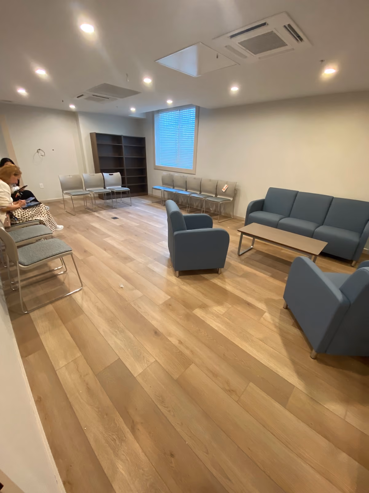 Spacious waiting room with blue seating, modern lighting, hardwood floors, and a window with natural light
