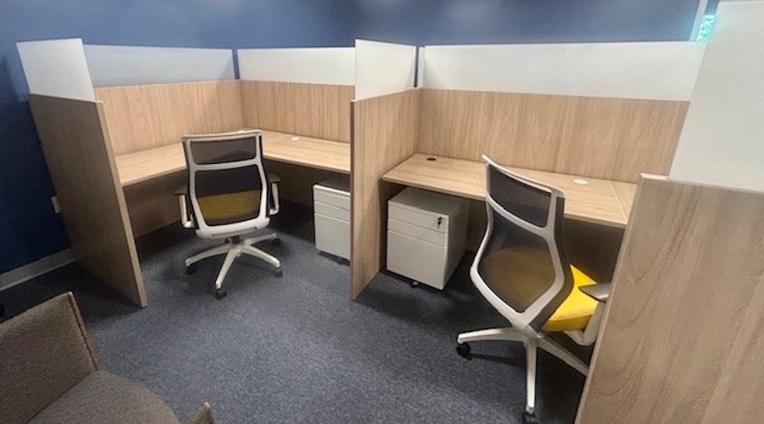 Two adjacent wood-paneled office cubicles with ergonomic chairs and natural lighting