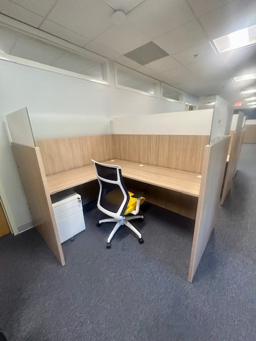 Private office cubicle with wood grain L-shaped desk, ergonomic chair, and drawer unit