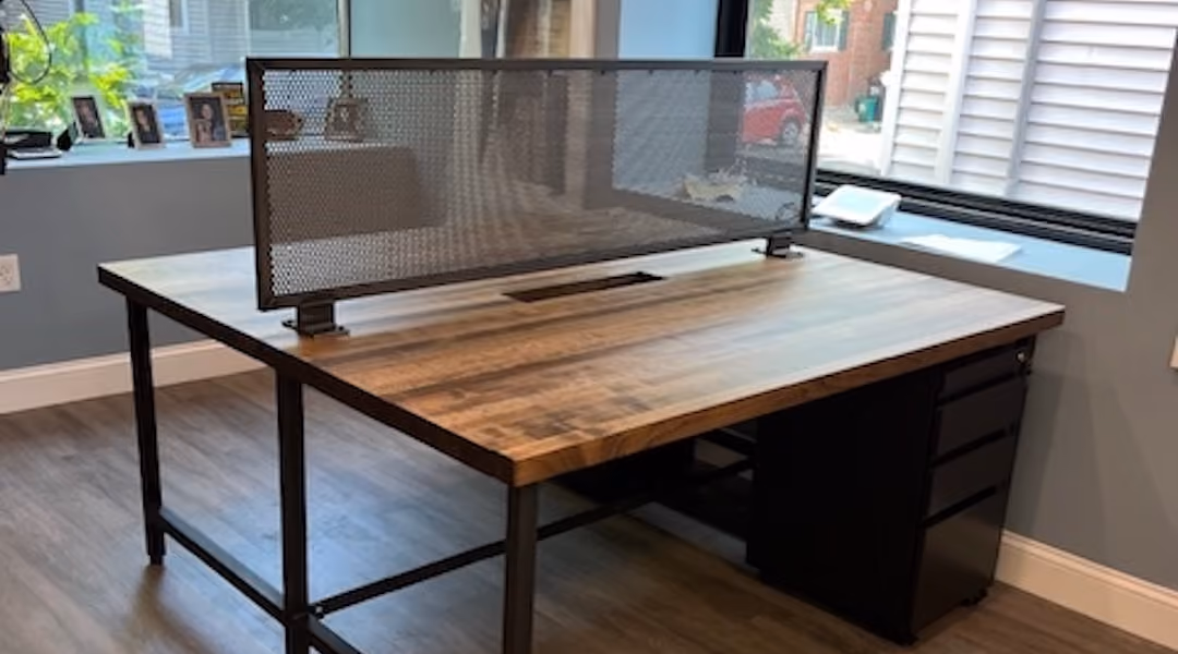 Modern industrial office desk with black metal legs, mesh privacy panel, and natural wood surface in bright workspace