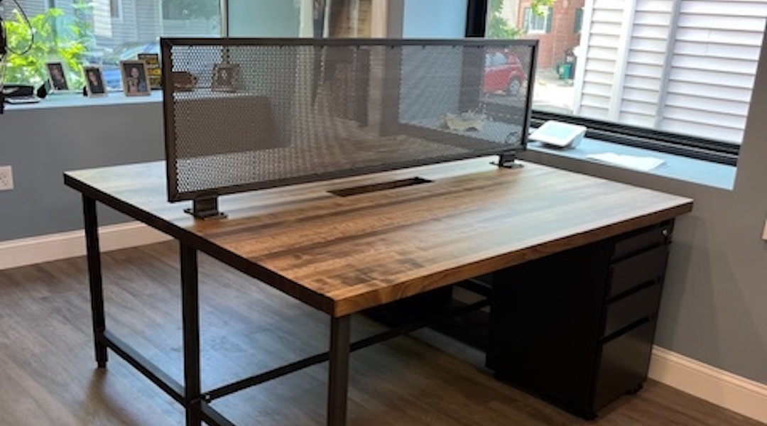 Modern industrial office desk with black metal legs, mesh privacy panel, and natural wood surface in bright workspace