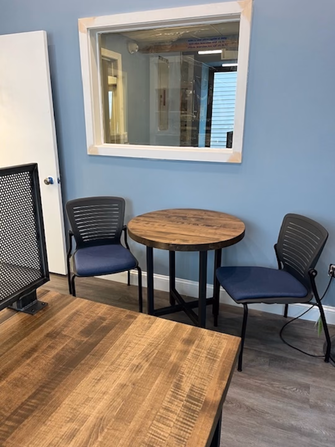 Cozy office corner with two blue guest chairs and small round wood meeting table against soft blue walls and wood flooring