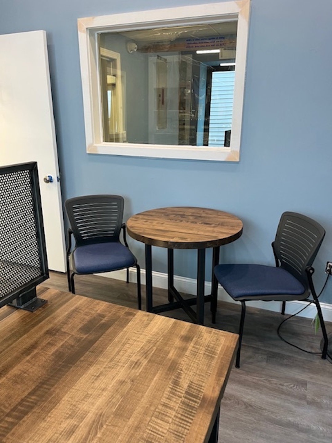 Cozy office corner with two blue guest chairs and small round wood meeting table against soft blue walls and wood flooring