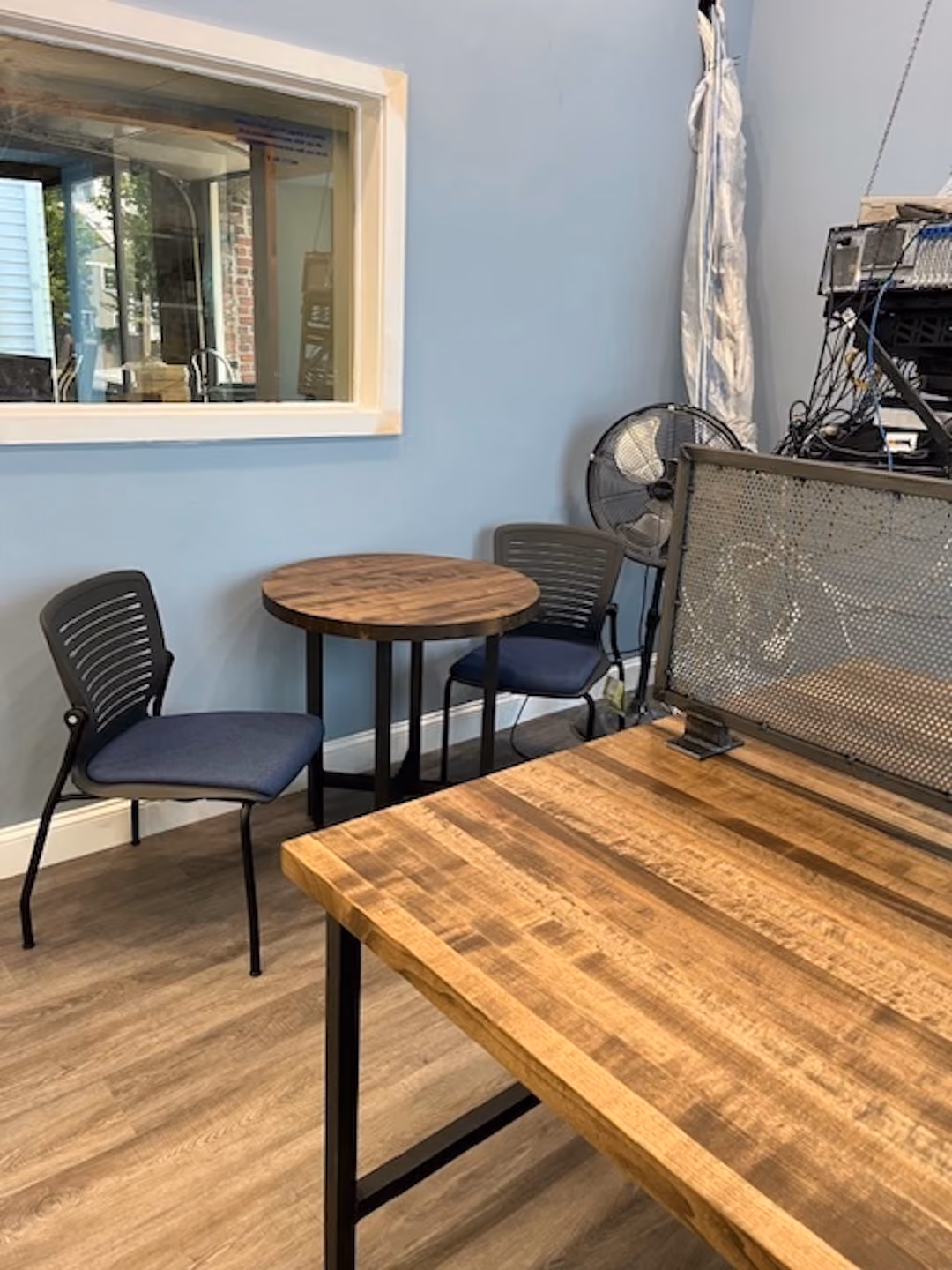 Contemporary shared office desk with metal privacy screen and natural wood top placed near interior window and blue wall