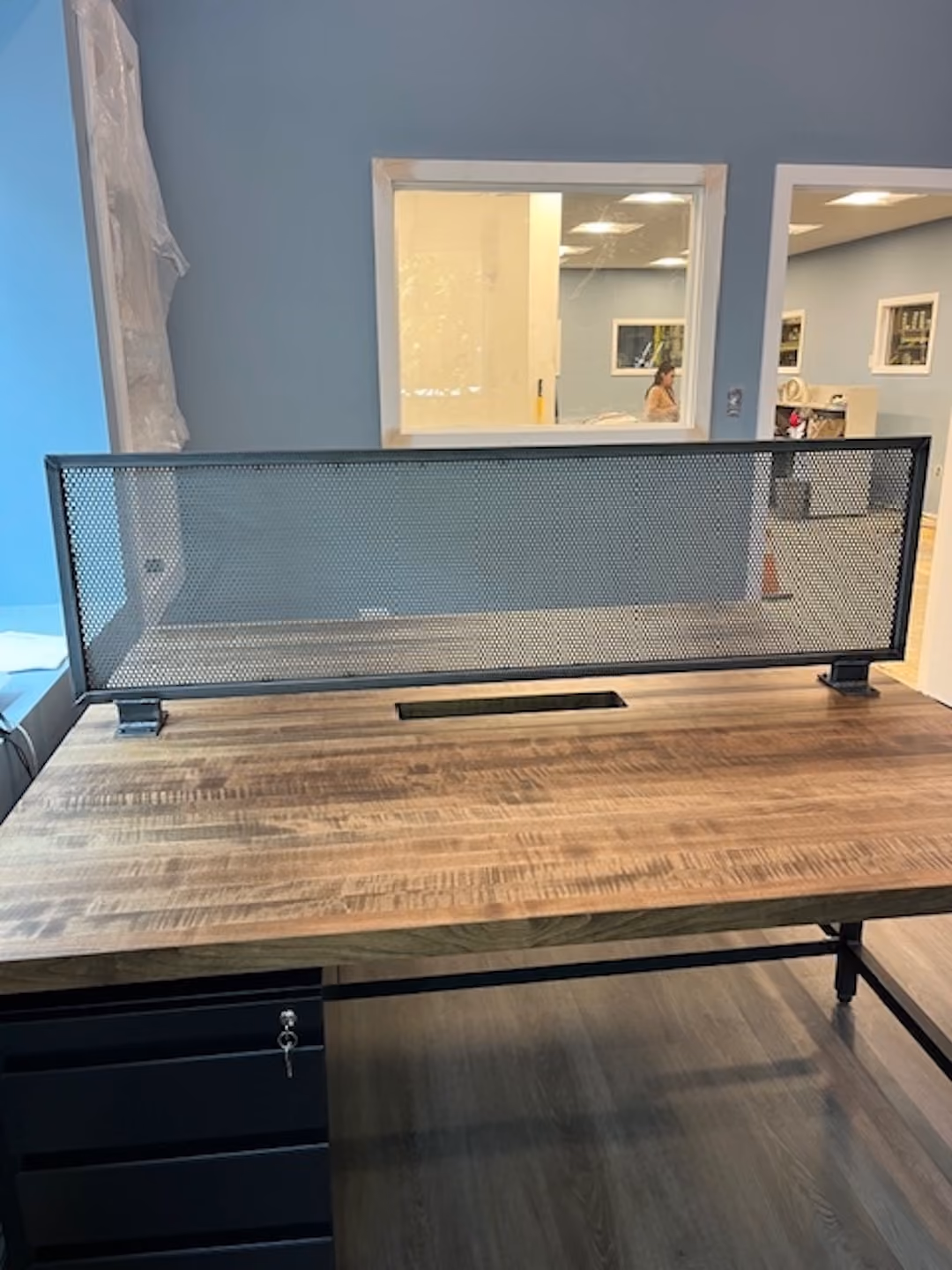 Close-up view of round wood cafe table with two guest chairs in modern office space with laminate wood flooring and blue wall