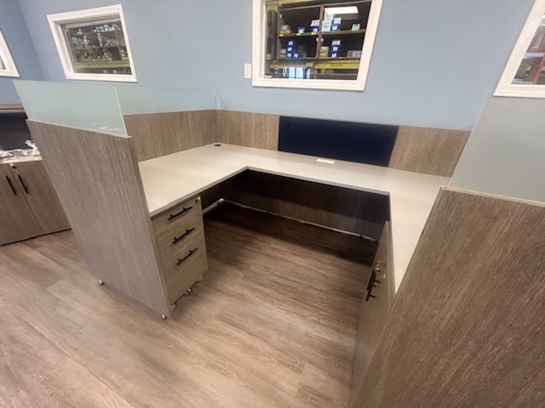 Modern L-shaped office cubicle with wood finish, glass privacy panels, and built-in drawers in a professional workspace.