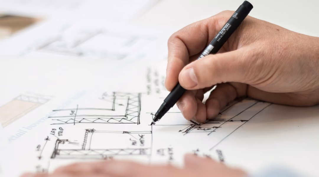 Designer holding a pen sketching an overhead layout in white paper.