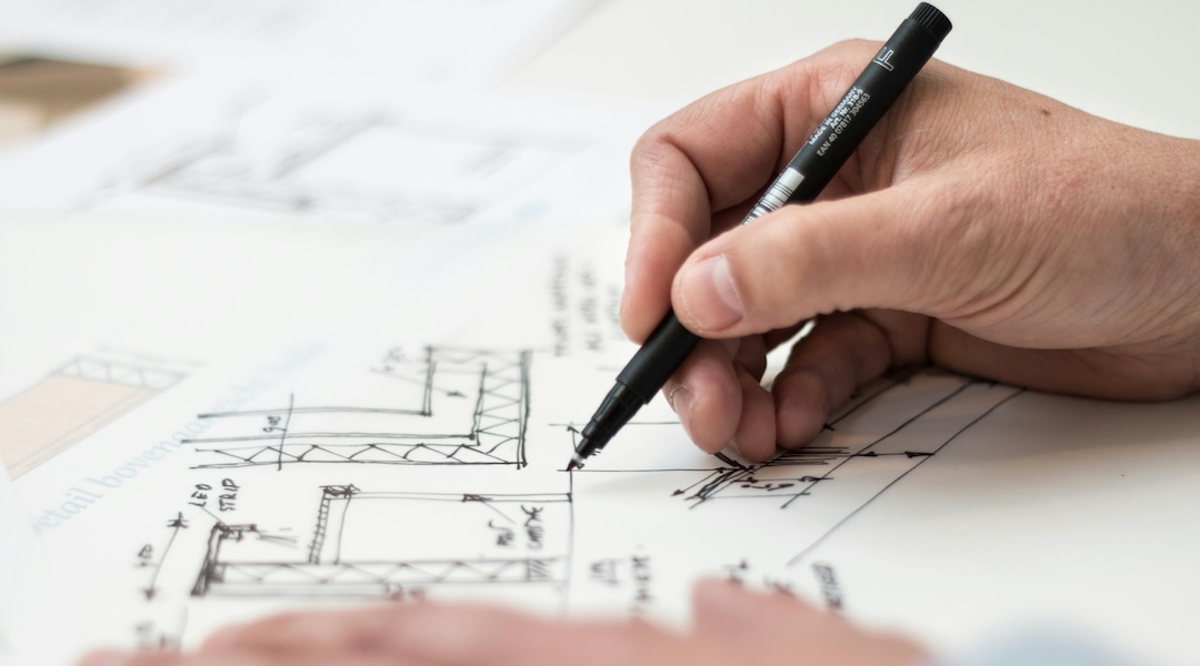 Designer holding a pen sketching an overhead layout in white paper.