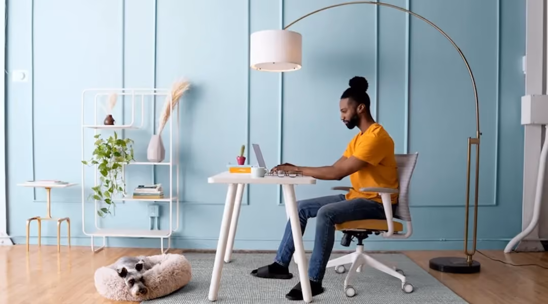 Man working at a small home office desk with dog resting