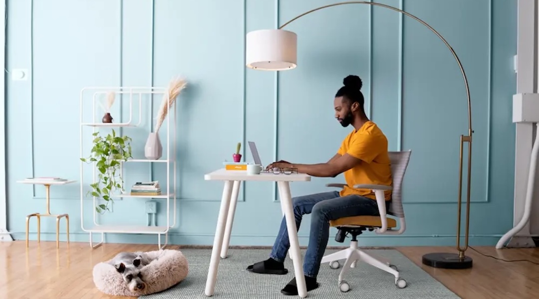 Man working at a small home office desk with dog resting