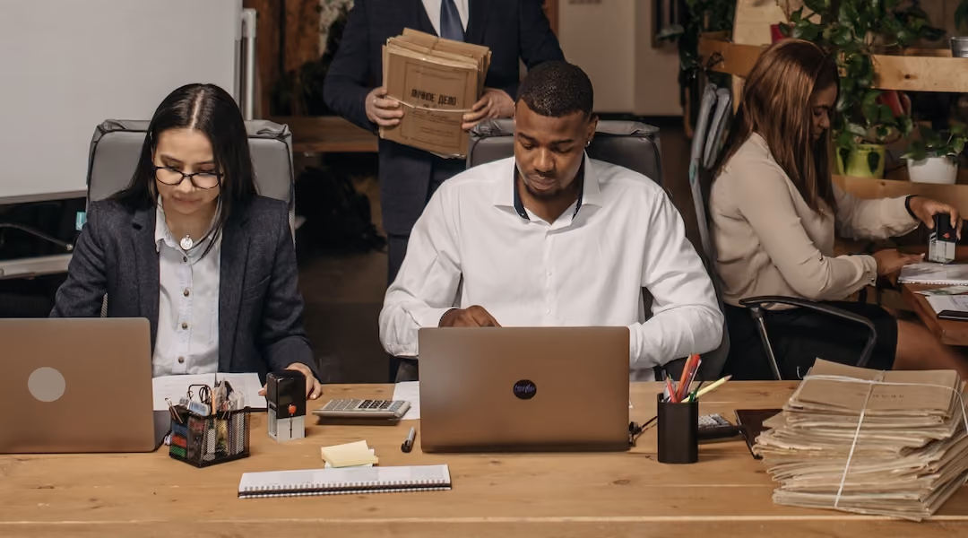 Diverse office team working on laptops and documents in an open-plan workspace.