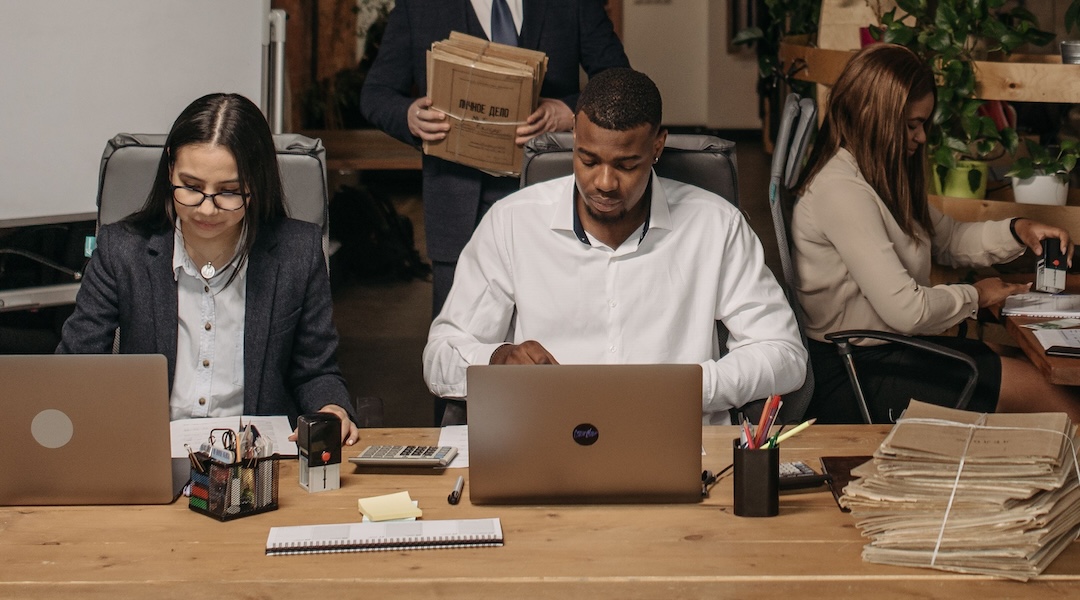 Diverse office team working on laptops and documents in an open-plan workspace.