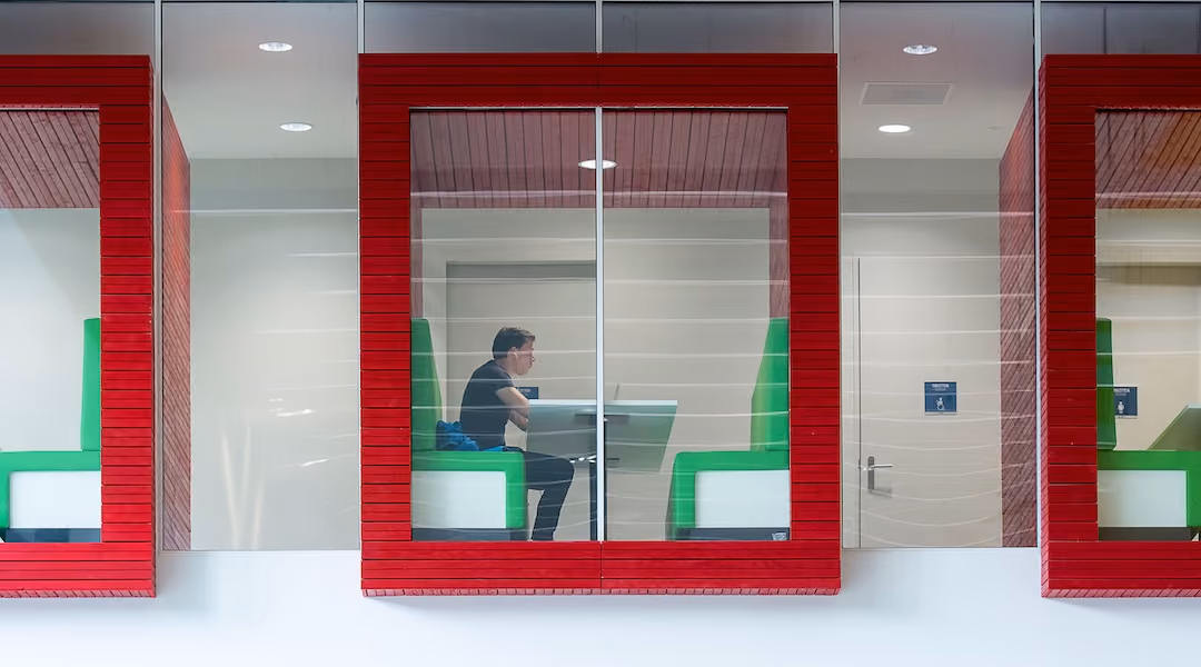 Contemporary coworking space with colorful booths and glass walls featuring a focused professional.