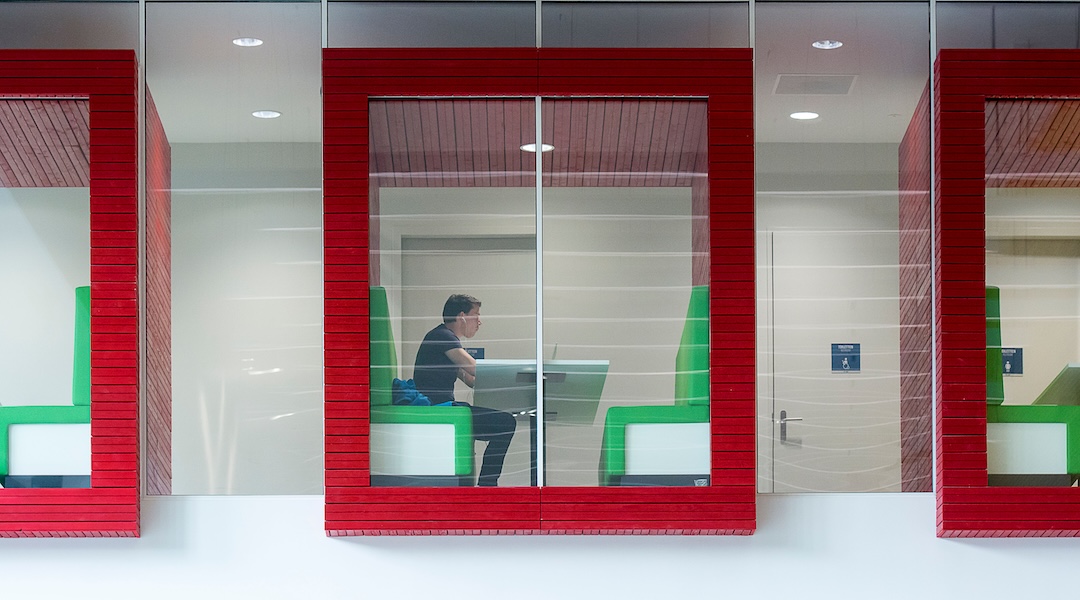 Contemporary coworking space with colorful booths and glass walls featuring a focused professional.