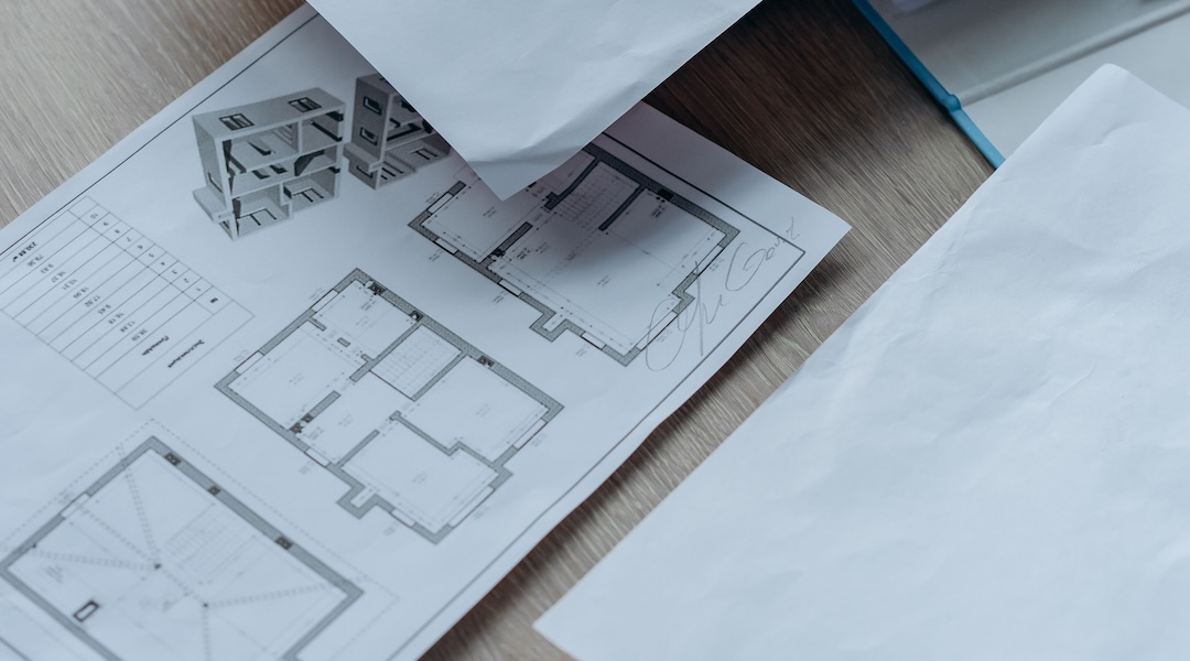 High angle view of architectural floor plans and paperwork on a wooden desk in an office setting.