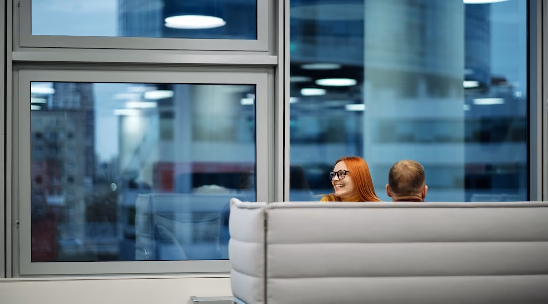Colleagues enjoying a casual discussion in a spacious office lounge with large windows.