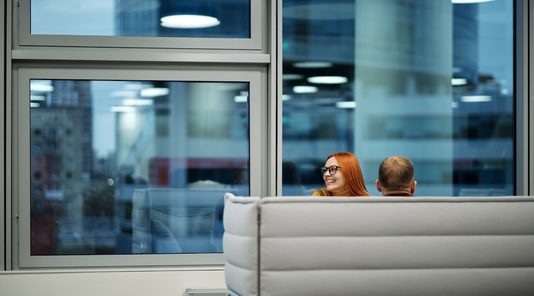 Colleagues enjoying a casual discussion in a spacious office lounge with large windows.