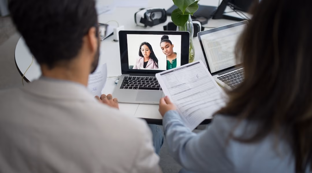 Two professionals conduct a virtual job interview using laptops in a modern office.
