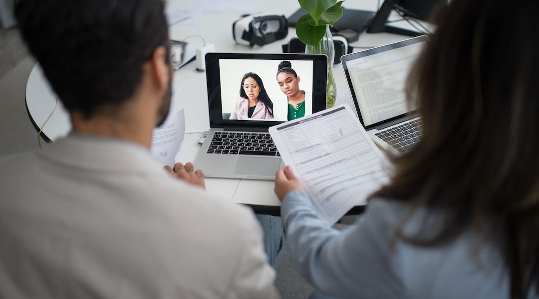 Two professionals conduct a virtual job interview using laptops in a modern office.