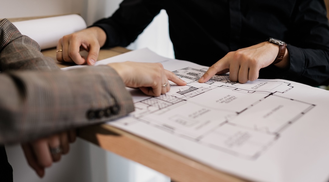 Two architects reviewing and pointing at a detailed floor plan on paper in an office setting.