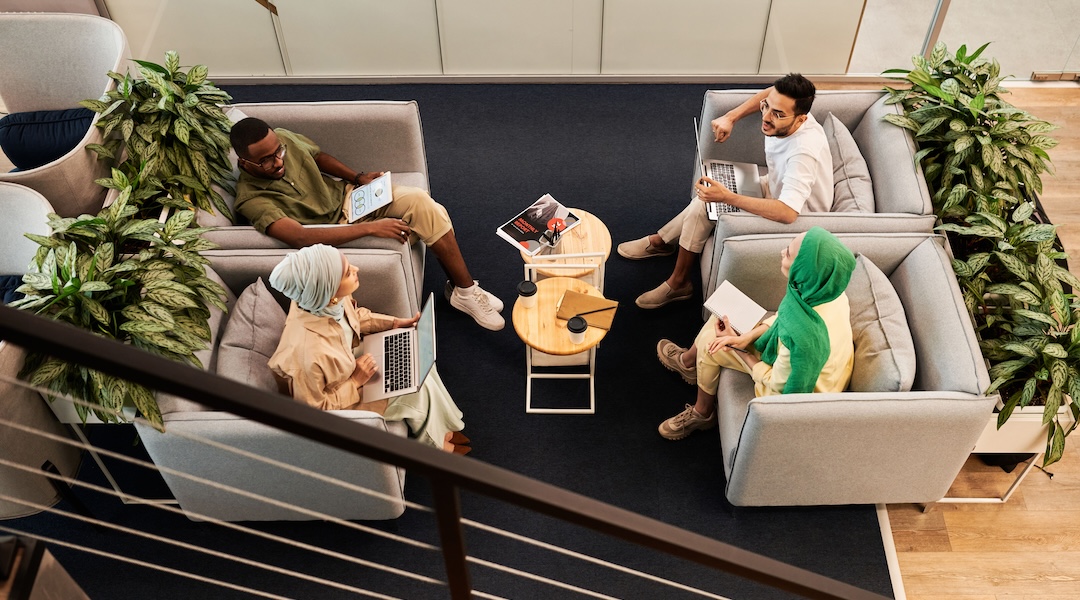 Overhead view of a diverse team engaging in a meeting in a modern office lounge area with laptops.