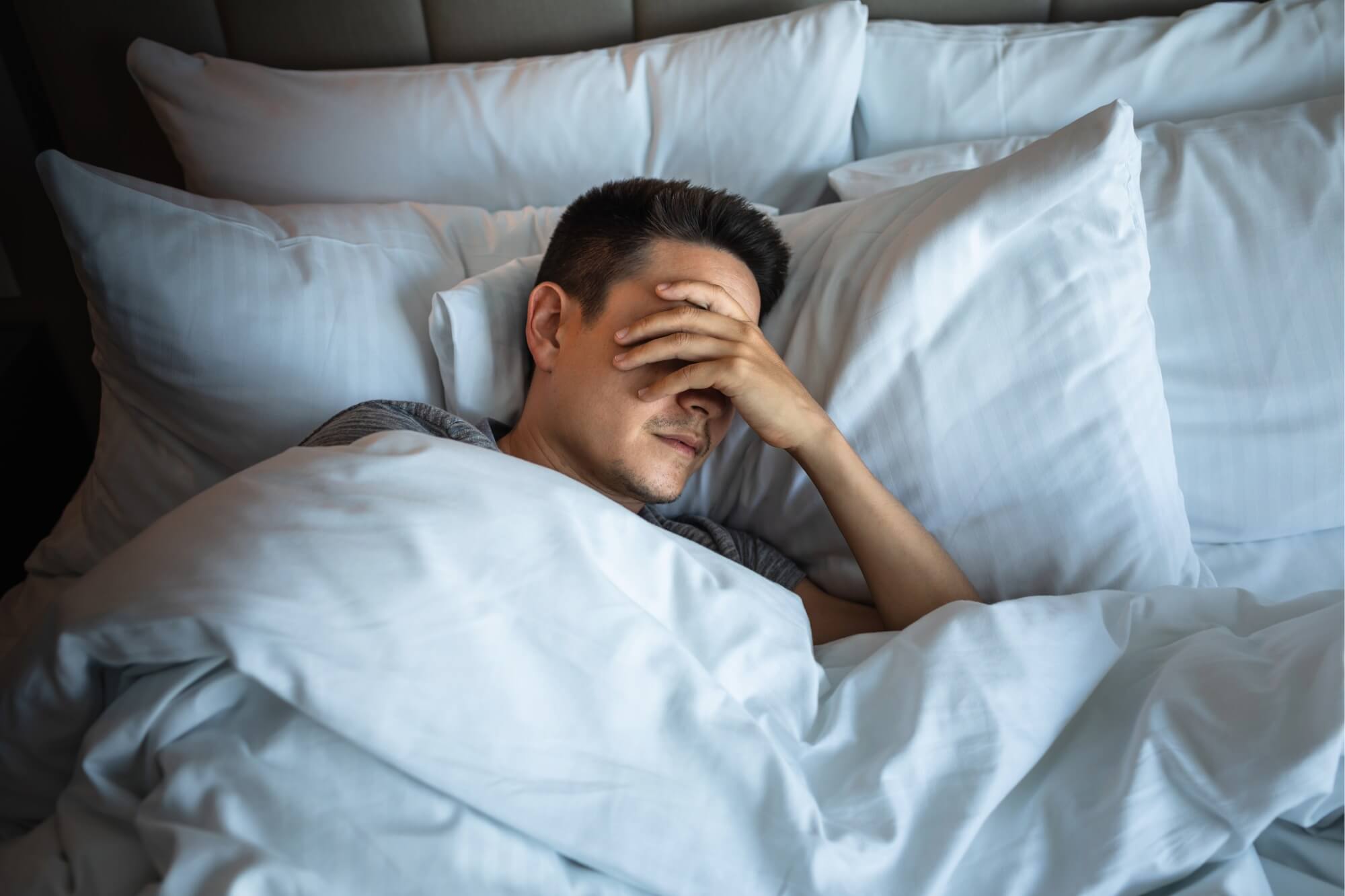 Man lying in bed with hand over face.