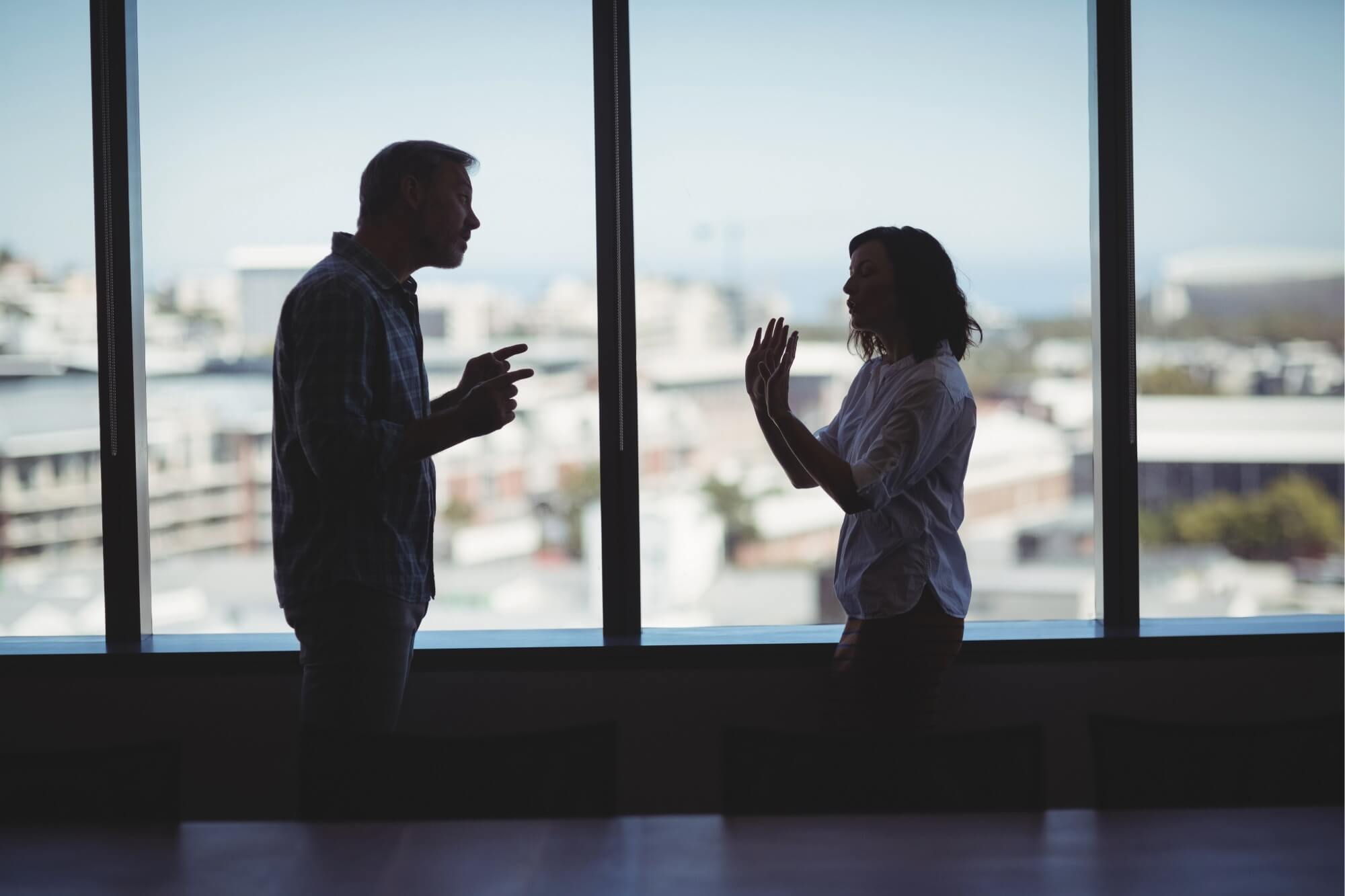 Two people silhouetted in disagreement indoors