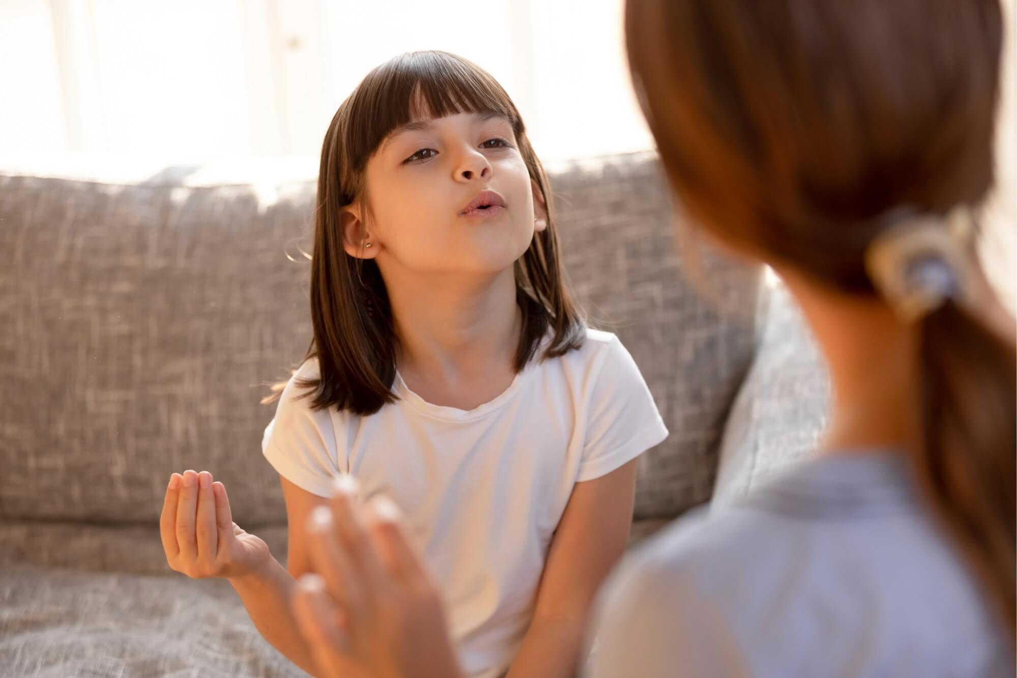 Child in white shirt speaking with a therapist on a gray sofa.