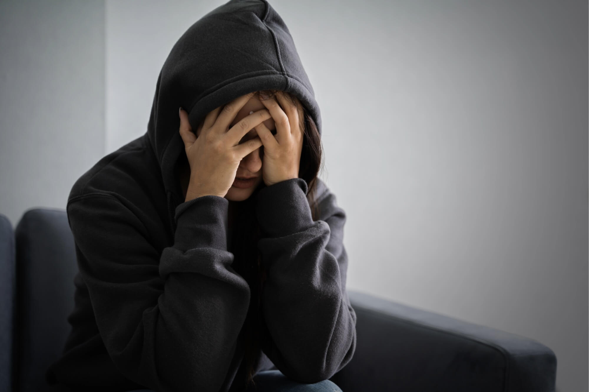 Person in dark hoodie sitting, holding head in hands, experiencing withdrawal symptoms.