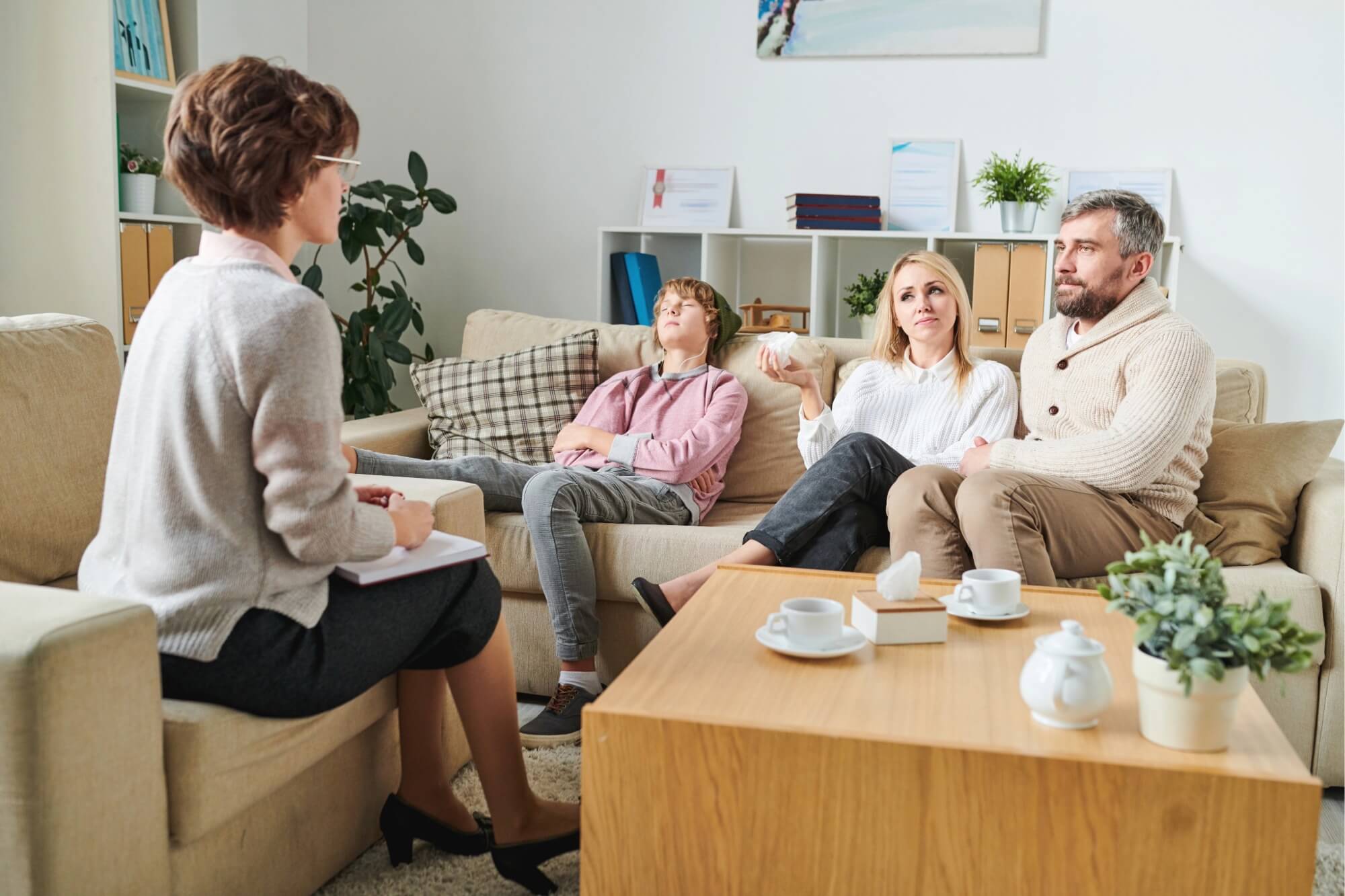 Man sitting on a sofa, appearing stressed, with hands clasped, in a counseling session.