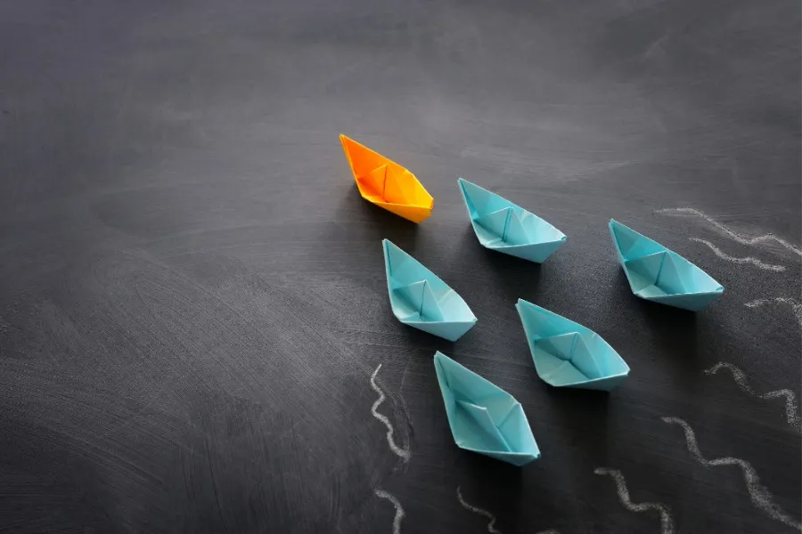 blue paper boats following an orange leading paper boat
