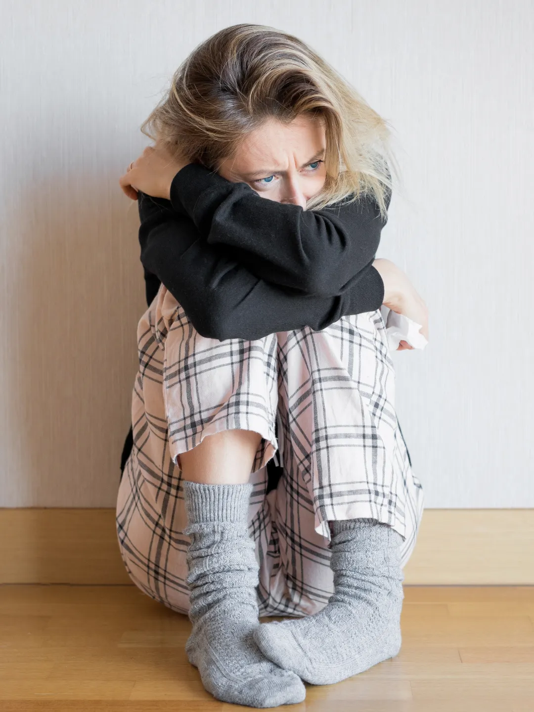 young girl with light wavy hair, curled up and huddled crossing hands looking sad or desoriented