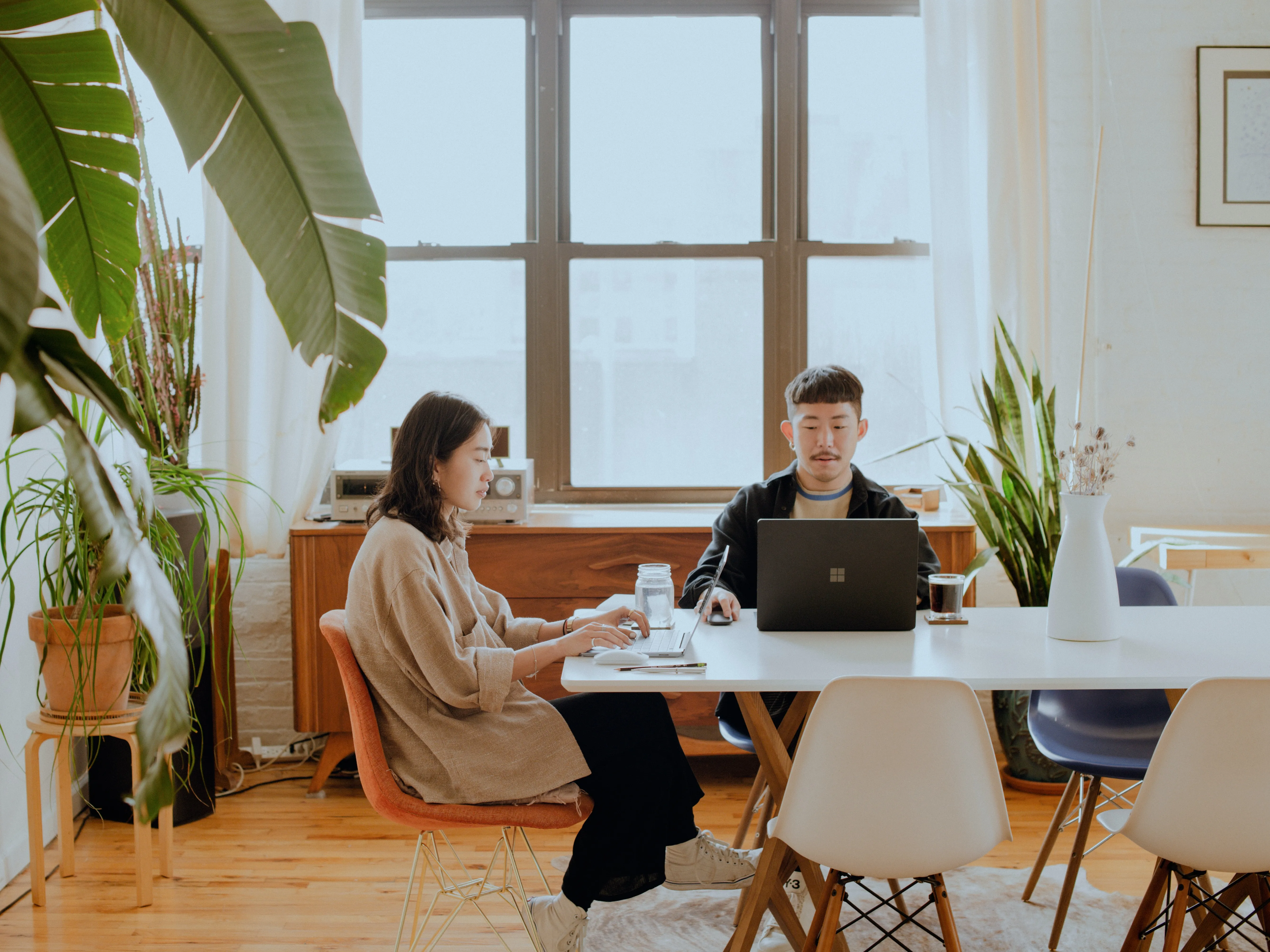two people working on laptops at a table in a bright room
