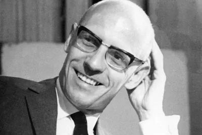 Retrato de Michel Foucault sorrindo, referência à sociedade disciplinar.