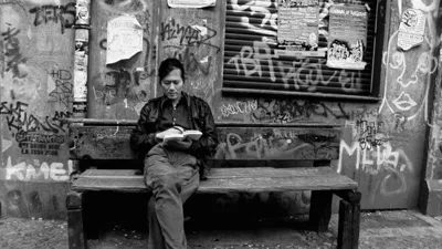 Trecho de documentário de Byung-Chul Han lendo um livro em banco de rua cercado por muros pichados.