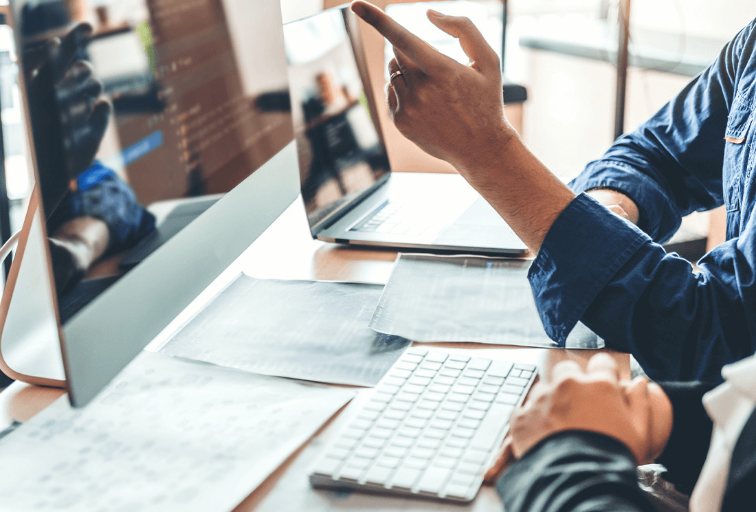 Softwareentwickler zeigt auf einen Bildschirm mit Programmcode am Arbeitsplatz