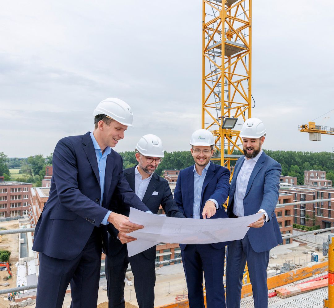 Vier Anwälte im Anzug mit Bauhelmen prüfen Baupläne auf einer Baustelle mit Kran