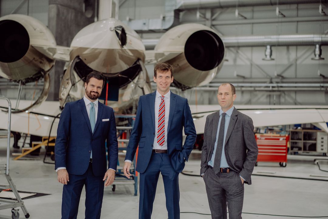 Drei Anwälte im Anzug vor einem Businessjet in einem Flugzeughangar