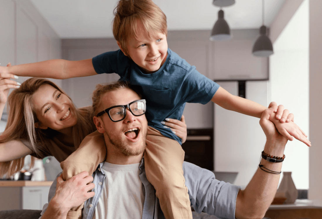 Glückliche Familie mit lachendem Kind auf den Schultern des Vaters zu Hause
