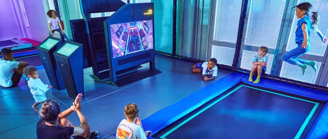 Two children playing ValoJump together on Trampolines. Spectators around are watching and cheering.
