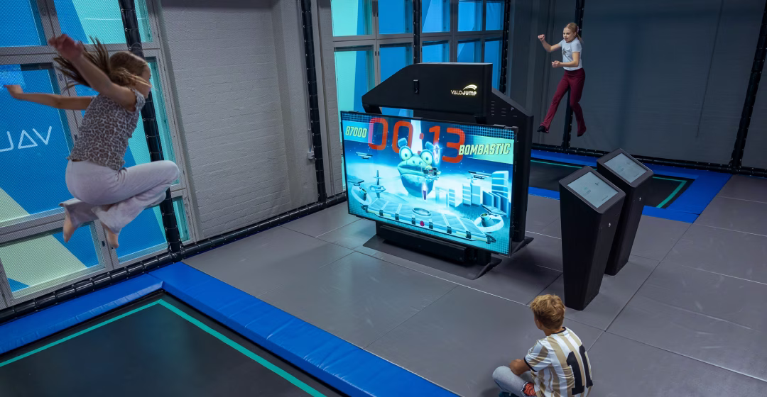 Two teenagers playing Stomp Squad on ValoJump, jumping high on the trampoline.