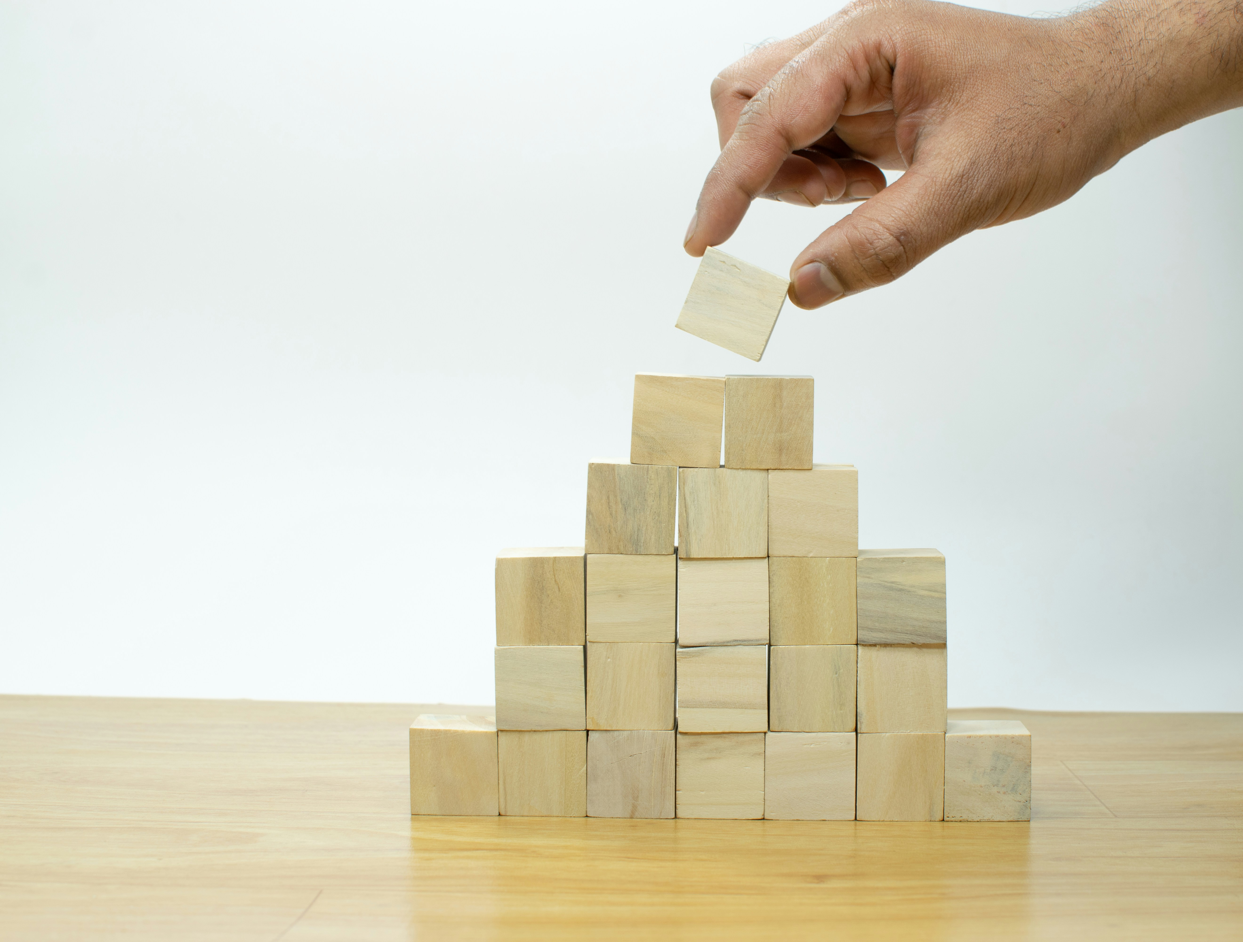 Hand placing a wooden block on a stacked pyramid of wooden cubes.