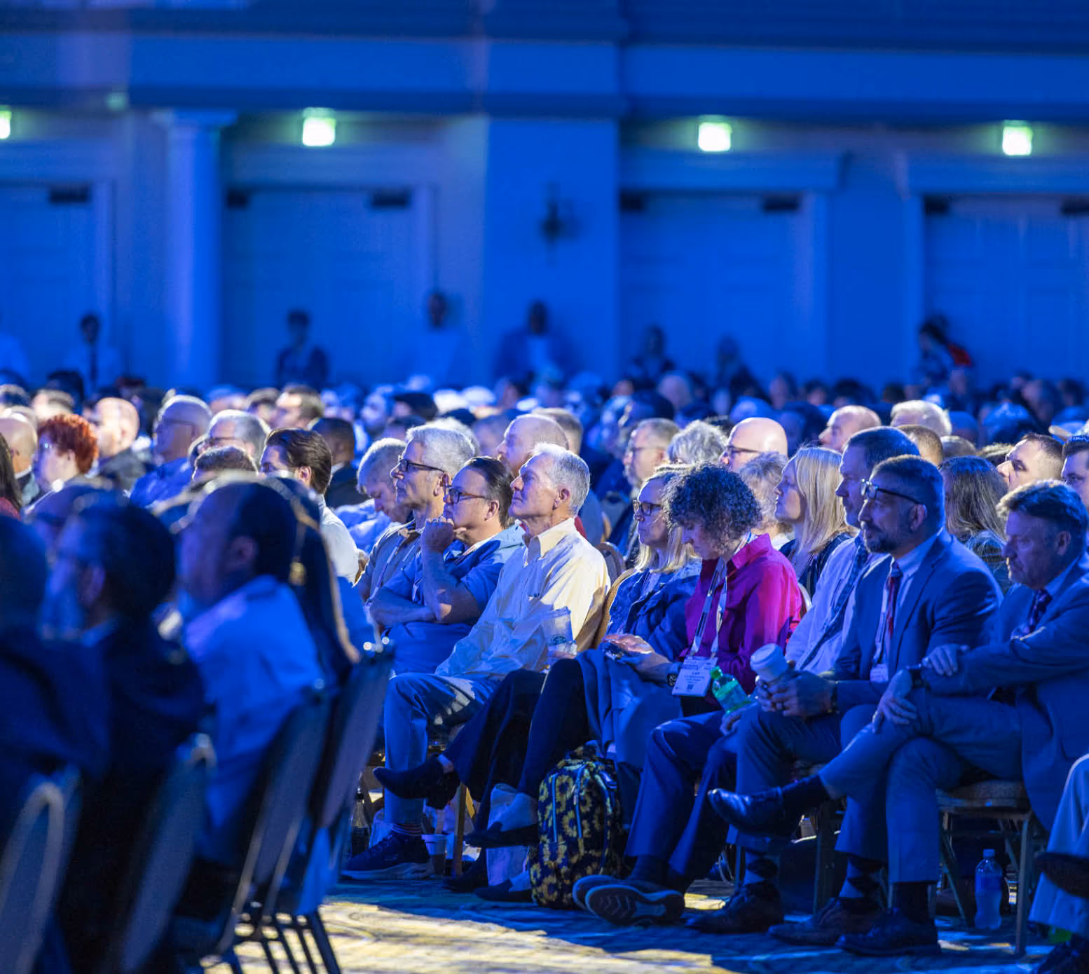 Audience members attentively listening at a formal event, seated at round tables with name tags.