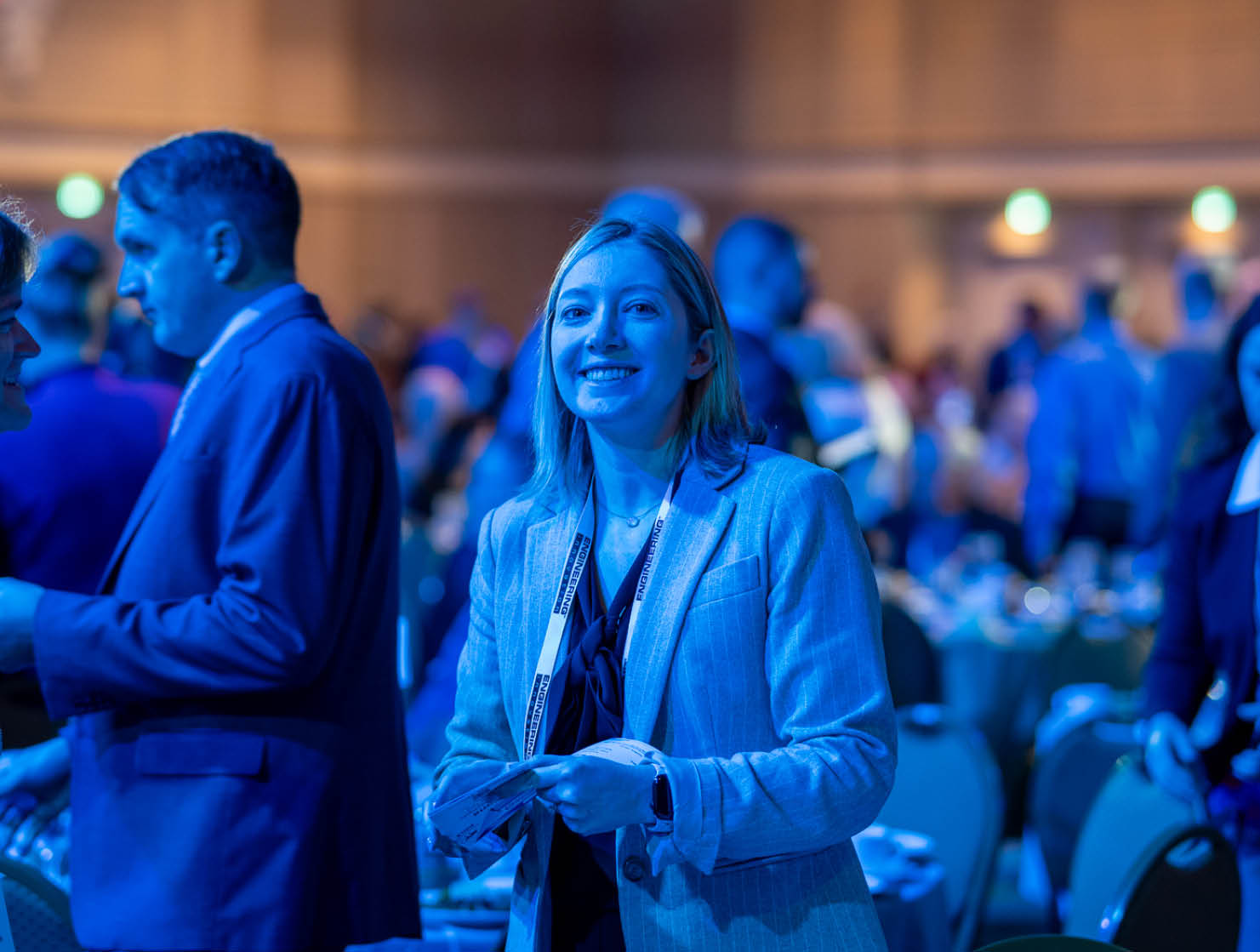 Audience members attentively listening at a formal event, seated at round tables with name tags.