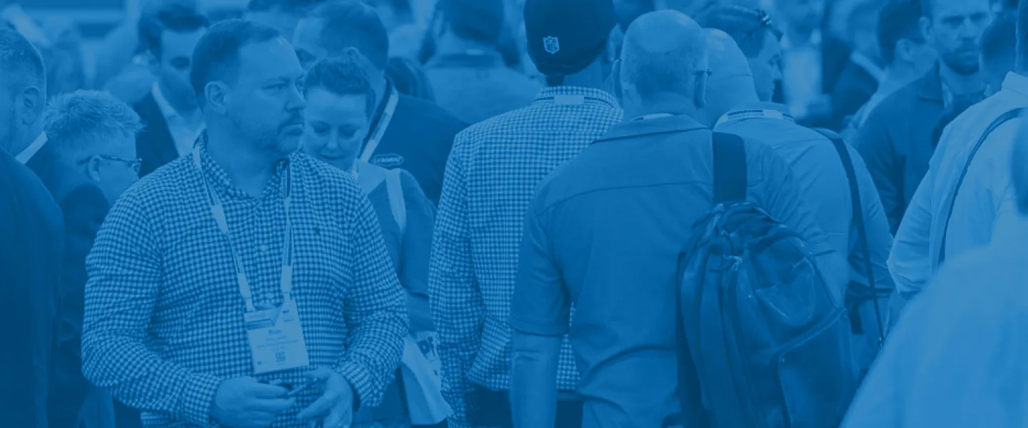 Crowd of people at an indoor event, with some wearing conference badges and carrying backpacks.