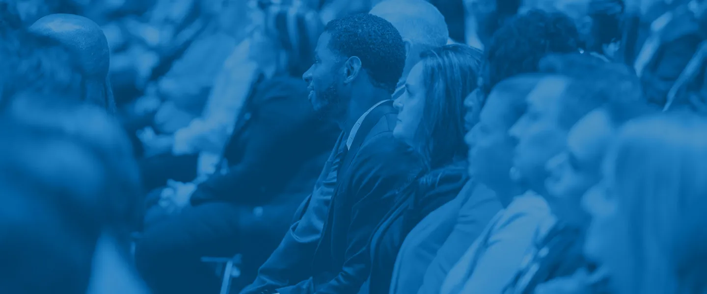 Audience of diverse adults attentively listening at an event with a blue overlay.