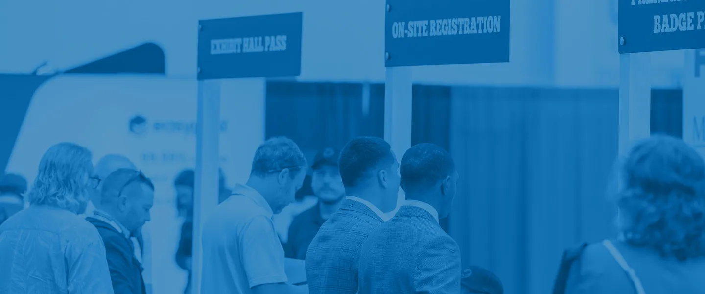 People waiting in line at registration booths labeled 'EXHIBIT HALL PASS' and 'ON-SITE REGISTRATION' at an indoor event.
