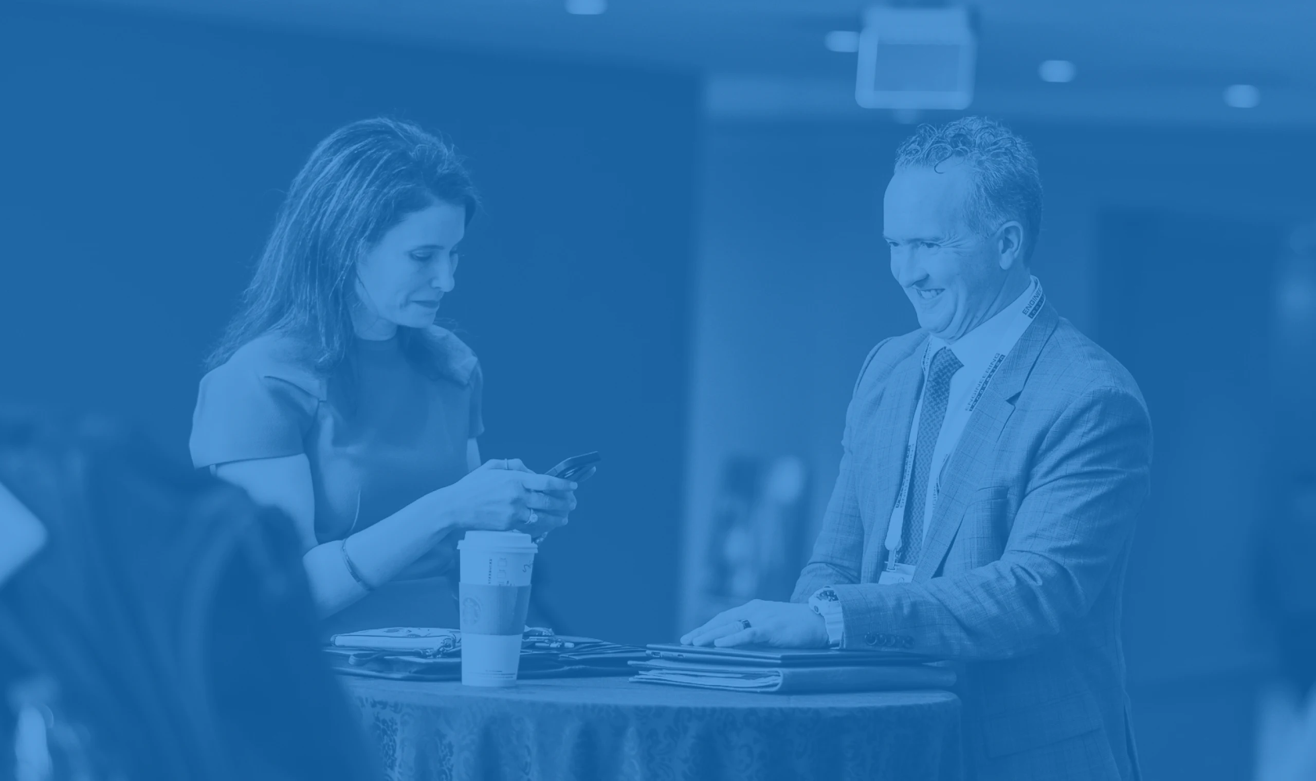 A woman in a green dress looks at her phone while a man in a suit and red tie smiles across a high table covered with a blue cloth.
